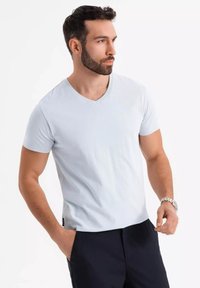 Vaaleansininen V-pääntie T-paita, joka on valmistettu pehmeästä puuvillasta, lyhyillä hihoilla ja slim fit -mallilla, yhdistettynä tummiin housuihin. Pintakuvioitu kangas on minimaalista muotoilua.