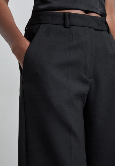 Sorte skræddersyede bukser i et glat stof, med en flad front, sidelommer og en slank silhuet. Der er også bæltestropper.