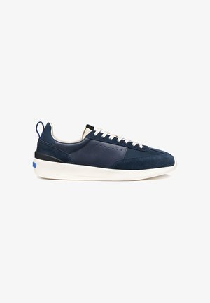 Marineblauwe sneaker met witte zool en veters, bovenwerk van suède en leer, zijventilatieluchtgaten en een hieltreklip met blauwe accenten.