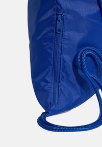 Modrá nylonová taška so zipsovým vreckom, guľatého tvaru a textúrovaným povrchom. Obsahuje pletené šnúrkové ramienka na nosenie.