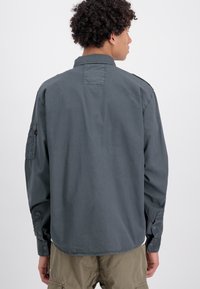 Gray long-sleeve shirt with a button-down collar, patch on left sleeve, and button cuffs; made of smooth fabric, casual design.