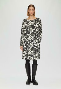 Robe florale noire et blanche avec des manches longues, un col rond et des poches, assortie à des bottes noires à hauteur de genoux. Tissu lisse avec un motif.