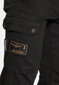 Zwarte cargobroek met een groot geborduurd patch met de tekst "LEADER 1" en een decoratieve Franse vlag. Duurzaam materiaal met meerdere zakken.