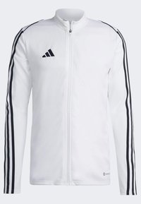 Witte zip-up jas van stof, met zwarte verticale strepen langs de mouwen en een geborduurd logo op de borst.