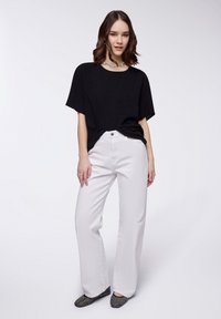 Maglietta nera oversize a maniche corte, pantaloni bianchi a gamba larga e ballerine nere a pois. Design semplice con scollatura rotonda e vestibilità rilassata.