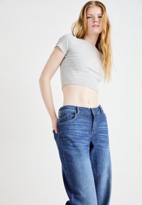 Γκρι ριγέ cropped τοπ συνδυασμένο με μπλε τζιν ψηλόμεσα παντελόνια. Τα τζιν διαθέτουν ελαφριά φθορά και τυπική λεπτομέρεια τσεπών.