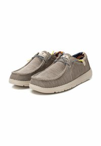 Zapatillas de lona beige tipo slip-on con un exterior texturizado, cordones elásticos y un interior con un colorido patrón. Cuentan con una suela de goma ligera.