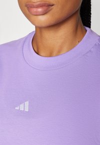 Μωβ βαμβακερό t-shirt με στρογγυλή λαιμόκοψη και μικρό λευκό λογότυπο με τρεις ρίγες στο μπροστινό μέρος, λεία υφή και χαλαρό σχέδιο.