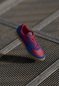 Nike sneakers med et blåt og pink design, tekstureret stof, flade snørebånd og en gul gummisål. Logoet er synligt på tungen.