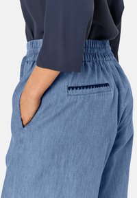 Pantalones de chambray azul claro con cintura elástica, bolsillos laterales y un bolsillo trasero con un detalle de borde ondulado.