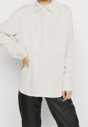 Person wearing light beige corduroy button-up shirt with long sleeves and collar, paired with black satin-like pants.