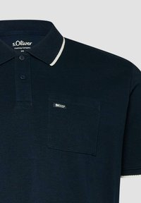 Polo bleu marine à manches courtes, patte de boutonnage à deux boutons, bordure blanche au col et aux manches, et une poche poitrine avec une petite étiquette.