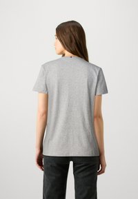 Camisa de algodón gris con mangas cortas y escote redondeado. Pequeño acento en rojo, blanco y azul en la parte posterior del cuello.