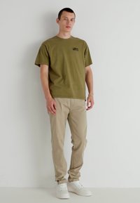 Green cotton t-shirt with black logo, beige trousers, white sneakers. Casual fit, plain design, minimal detailing, and soft texture.