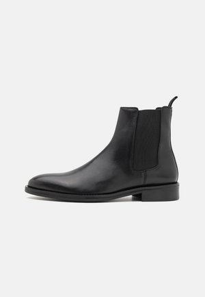Schwarze Leder-Chelsea-Stiefel mit elastischen Seitenpaneelen, abgerundeter Spitze, Zugschlaufe und flacher Gummisohle. Glatte Textur und elegantes Design.