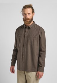 Bruine lange mouwen shirt met knoopsluiting aan de voorkant, twee borstzakken en een kraag. De stof heeft een gestructureerde afwerking en een relaxte pasvorm.