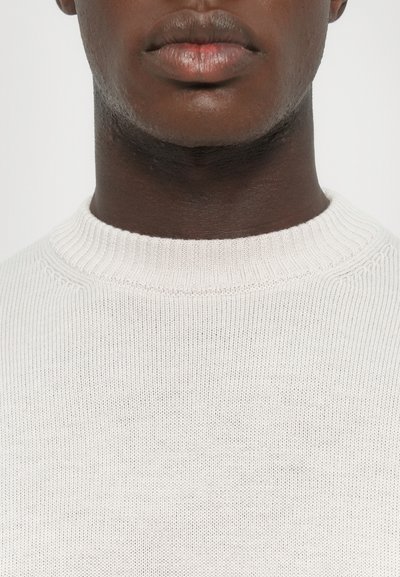 White knit sweater with a ribbed round neck, featuring a textured pattern and subtle stretch, showcasing a close-up view of the collar area.