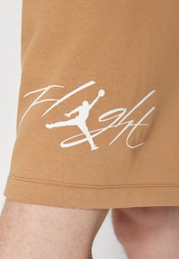 Tissu beige avec un graphisme blanc d'un joueur de basket sautant et le mot « Flight » en lettres cursives.
