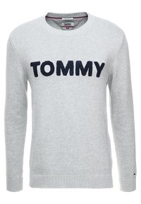 Maglione lavorato a maglia grigio chiaro con il testo "TOMMY" in blu navy sul petto, polsini e orlo a coste, e scollatura rotonda.