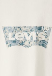 Bijela tkanina sa plavim i bijelim uzorkom logotipa Levi's unutar karakterističnog oblika štita, sa simbolom registrirane marke.
