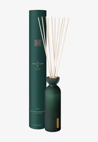 Vase vert à nervures avec un cou étroit contenant des tiges en bois, accompagné d'une boîte cylindrique verte haute étiquetée "Le Rituel de Jing."