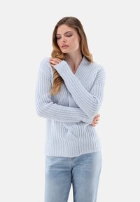 Helles blaues Strickpullover mit strukturiertem Rippdesign und V-Ausschnitt. Lange Ärmel mit engen Bündchen. Kombiniert mit hellen Denim-Jeans.