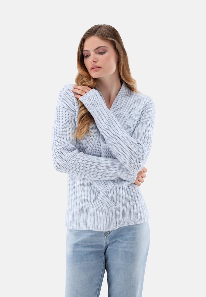 Helles blaues Strickpullover mit strukturiertem Rippdesign und V-Ausschnitt. Lange Ärmel mit engen Bündchen. Kombiniert mit hellen Denim-Jeans.
