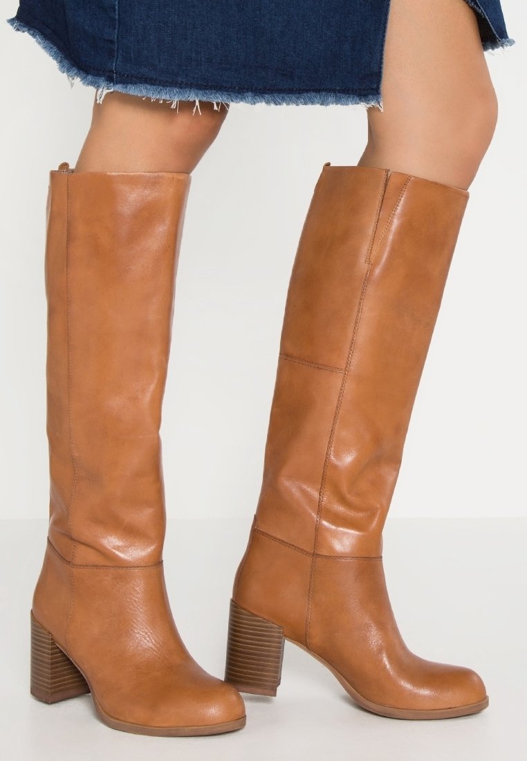 Bottes en cuir tan jusqu'aux genoux avec un design légèrement affaissé, des talons blocs et des accents en bois texturé. Bout arrondi et finition lisse.