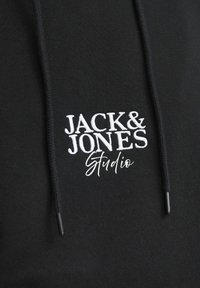 Schwarzer Hoodie mit einem weißen gestickten Logo, das "JACK & JONES Studio" zeigt, ausgestattet mit einer Kordel und einer glatten Stofftextur.