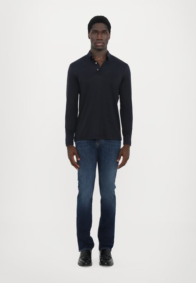 Ναυτικό μπλουζάκι με μακριά μανίκια συνδυασμένο με μπλε τζιν παντελόνι και μαύρα παπούτσια. Το μπλουζάκι διαθέτει γιακά και κουμπιά στο λαιμό.