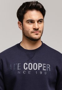 Granatowy sweatshirt z okrągłym dekoltem, teksturowanym materiałem i kontrastowym nadrukiem "LEE COOPER SINCE 1908" w wyraźnych, grubych literach.