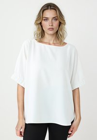 Witte blouse met een relaxte pasvorm, brede bootnek en korte puffmouwen. Gladde stof met een subtiele glans, zonder patronen of versieringen.