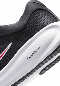 Κοντινή λήψη της φτέρνας ενός μαύρου αθλητικού παπουτσιού Nike με λευκή σόλα και την ετικέτα "ComfiRide" καθώς και το λογότυπο Swoosh σε κόκκινο και άσπρο χρώμα πάνω σε υφασμάτινο πλέγμα.