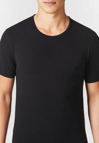 T-shirt nera a maniche corte realizzata in morbido cotone, con scollatura rotonda e design aderente. Tessuto liscio senza motivi visibili.
