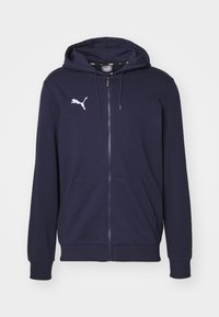 Námořnická modrá mikina na zip vyrobená z měkkého materiálu, s klokánkovou kapsou a bílým logem Puma na levé části hrudi. Kapuce s nastavitelnou šňůrkou.