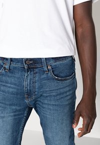 Mörkblå denimjeans med klassisk passform, med knapp och dragkedja, fem fickor och subtil blekning. Matchas med en vit t-shirt.
