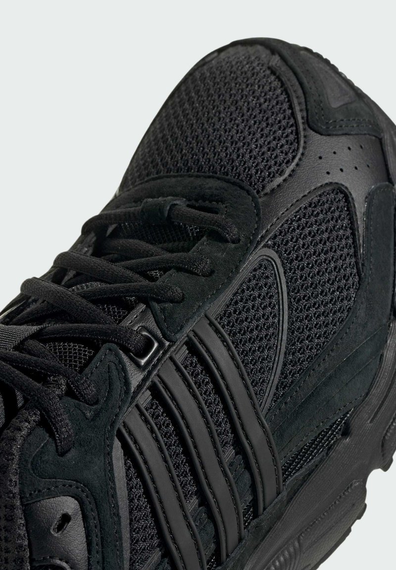 Scarpa sportiva nera con tomaia in rete, accenti in suede e sovrapposizioni sintetiche. Presenta lacci piatti e suola in gomma testurizzata.