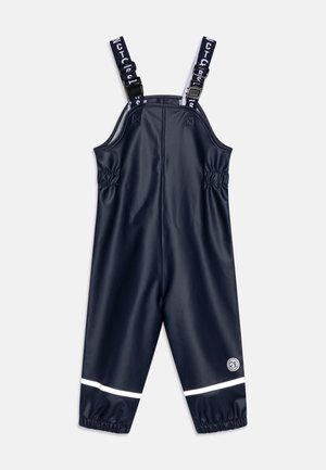 Salopette imperméable marine avec bretelles ajustables, taille élastiquée et bande réfléchissante blanche en bas. Texture lisse.