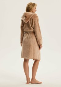 Beżowy, kąpielowy szlafrok z kapturem, wykonany z miękkiego, pluszowego materiału. Posiada wiązany pas, długie rękawy oraz długość do kolan. Gładka faktura.