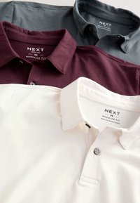 Trois polos pliés en blanc, bordeaux et gris foncé, chacun étiqueté de la marque Next, taille medium, coupe régulière.