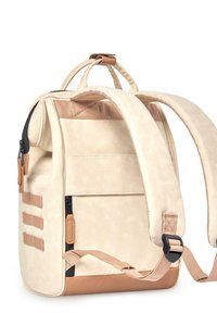 Mochila de tela beige con un acabado texturizado, correas ajustables y una base de cuero marrón. Cuenta con múltiples bolsillos con cremallera y cintas de web en los laterales.