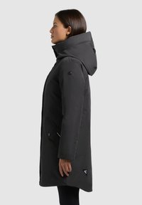 Mustmust mustkoot, millel on kapuuts, küljetaskud ja logokleeps. Sile, matt kangas, voolujooneline siluett ja kindlad kinnitused.