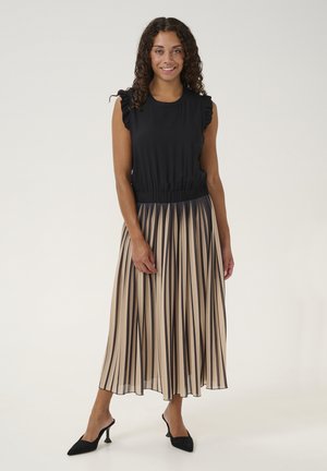 Top negro sin mangas con hombros con volantes, combinado con una falda plisada beige con rayas marrones. La modelo lleva tacones negros de punta.