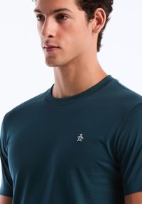 Donkerblauwe korte mouwen t-shirt van zachte stof, met een klein wit pinguïnlogo op de linkerborst. Ronde halsontwerp.