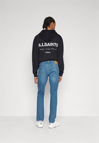 Un hoodie negro corto con texto blanco, jeans azulados ajustados y zapatillas blancas. El hoodie tiene un cordón y un bolsillo tipo canguro.
