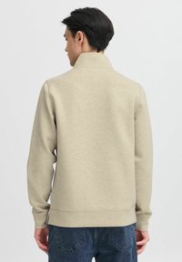 Lys beige, bomullsblanding genser med høy hals, lange ermer og en avslappet passform. Har sidesplitter nederst og ribbestrikkede mansjetter.
