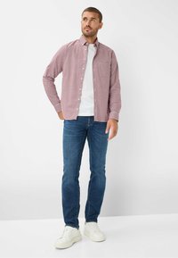 Rot und weiß karierte Langarmbluse über einem weißen T-Shirt, kombiniert mit blauen Jeans und weißen Sneakern. Einheitlicher Hintergrund.