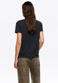 Czarna koszulka z krótkim rękawem ozdobiona małymi metalicznymi kropkami. Połączona z luźnymi, zielonymi spodniami w wzory.