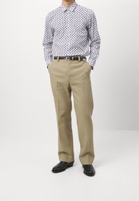 Witte shirt met marineblauwe stippen, tan geklede broek met plooien, zwarte riem met zilveren accenten en zwarte leren schoenen.