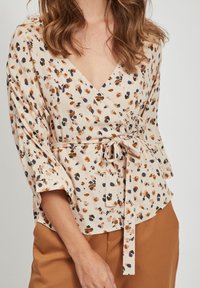 Haut à motifs floraux en crème avec des éclats marron, orange et bleu marine. Présente un décolleté en V plongeant et un détail de taille à nouer. Tissu doux avec des manches amples.